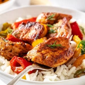 a white bowl with rice and sauteed chicken and bell peppers on top.