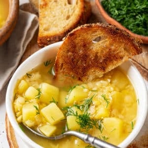 split-pea-soup-in-a-white-bowl-with-a-spoon-in-it-and-toast-slices-all-on-a-wooden-board