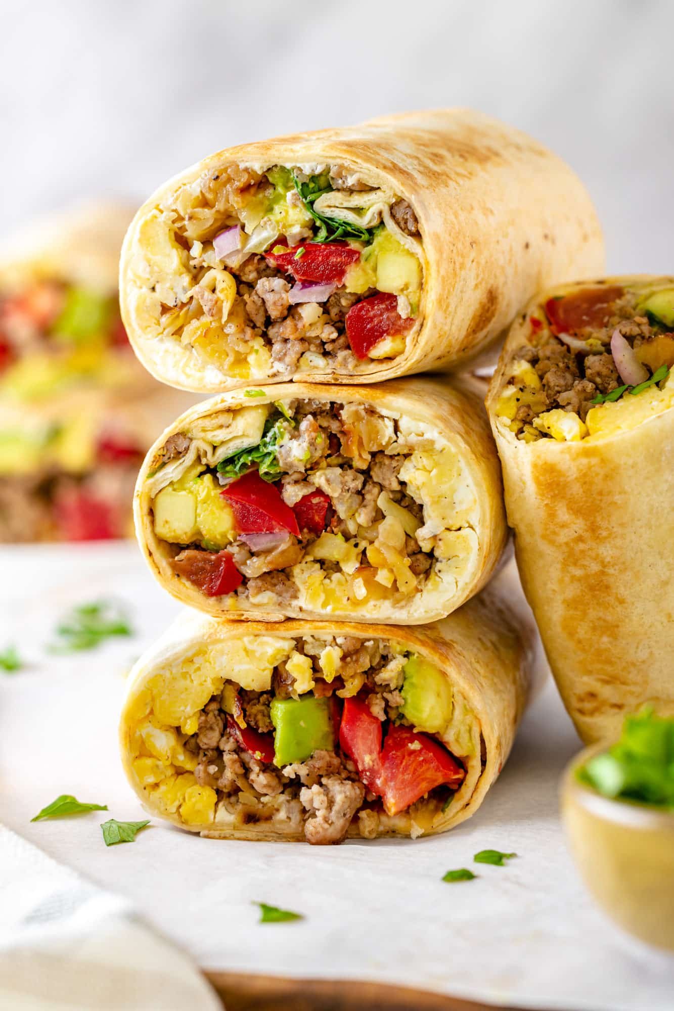 A stack of breakfast burritos with another burrito half leaning on the side.