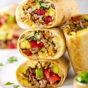 A stack of breakfast burritos with another burrito half leaning on the side.