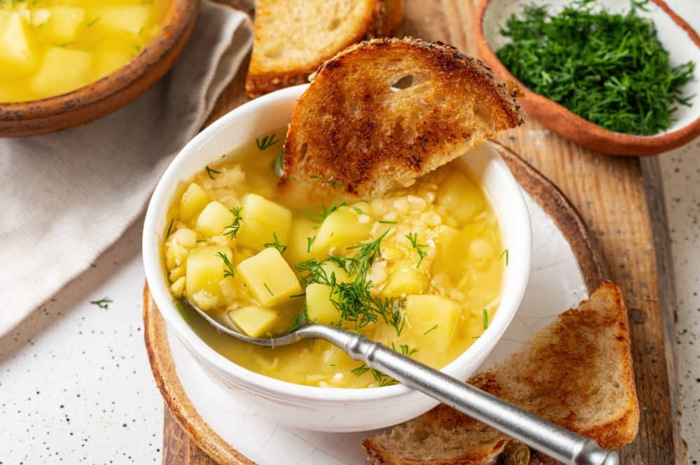 split-pea-soup-in-a-white-bowl-with-a-spoon-in-it-and-toast-slices-all-on-a-wooden-board