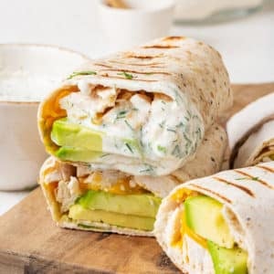 Stacked and halved grilled chicken avocado wraps with ranch on the side.