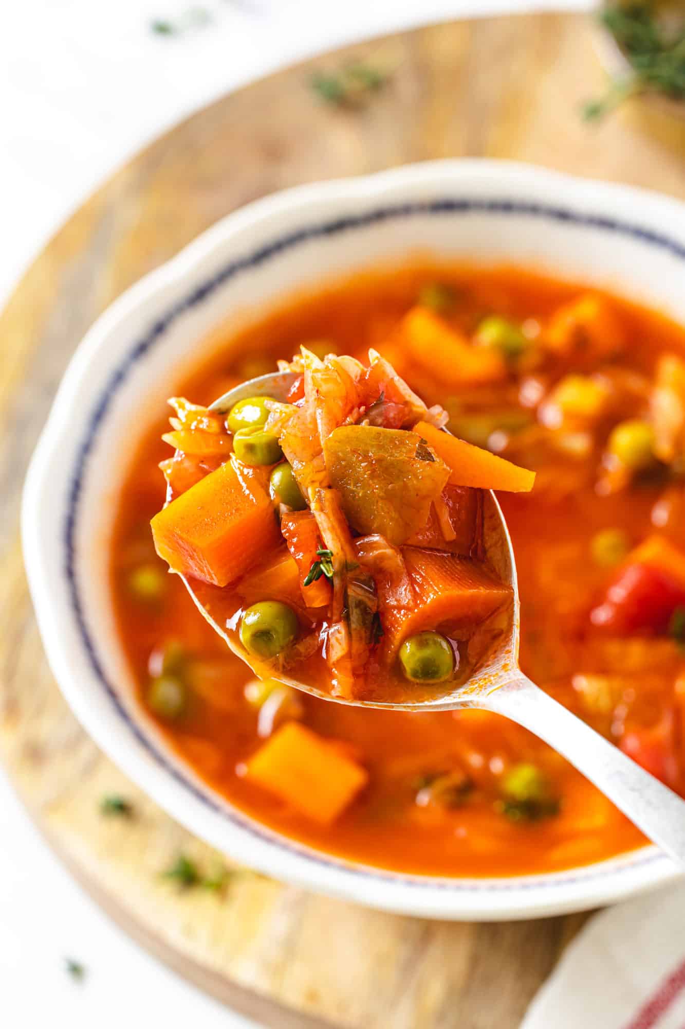 A spoon with vegetable soup and a bowl in the background.