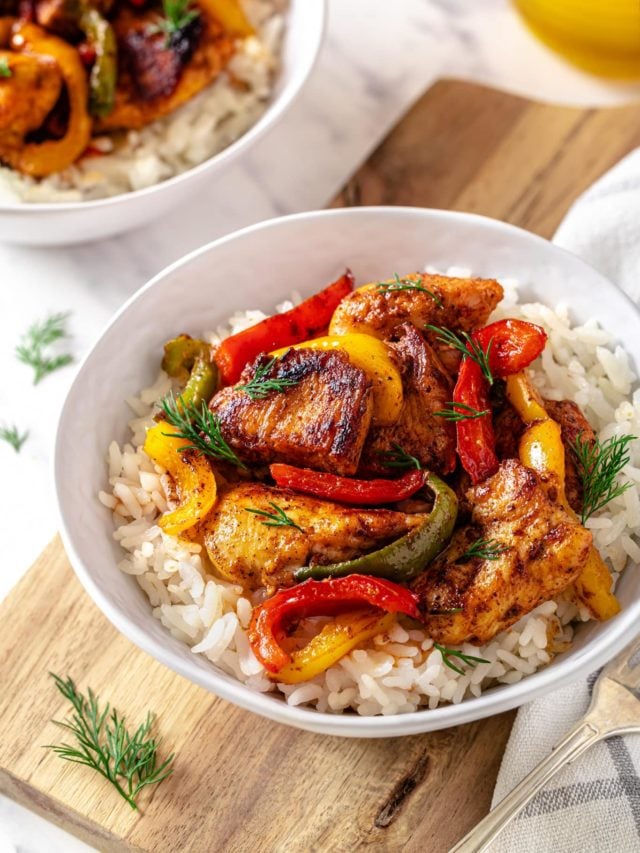 chicken and bell peppers all cooked together in a rice bowl with greens around.