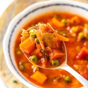 a vegetable soup on a spoon and in a bowl on a wooden board.