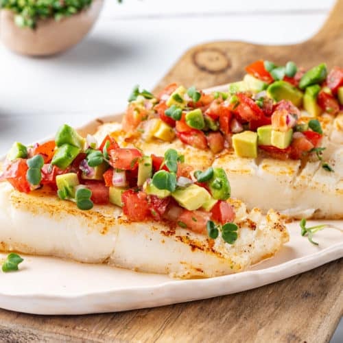 halibut-with-salsa-on-a-white-plate-on-a-wooden-board-with-a-fork-on-the-side