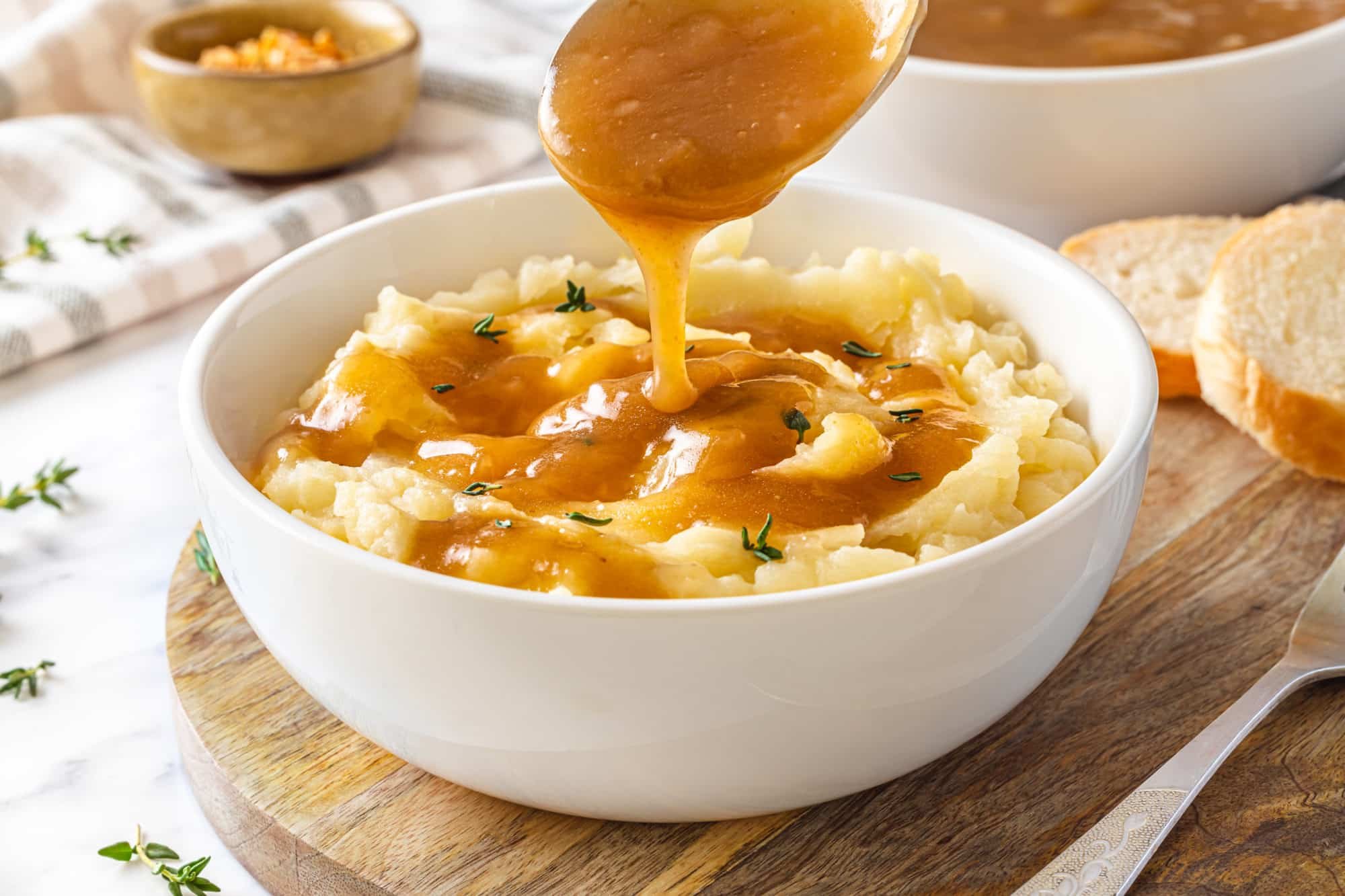 adding gravy onto a bowl of mashed potatoes with a ladle.