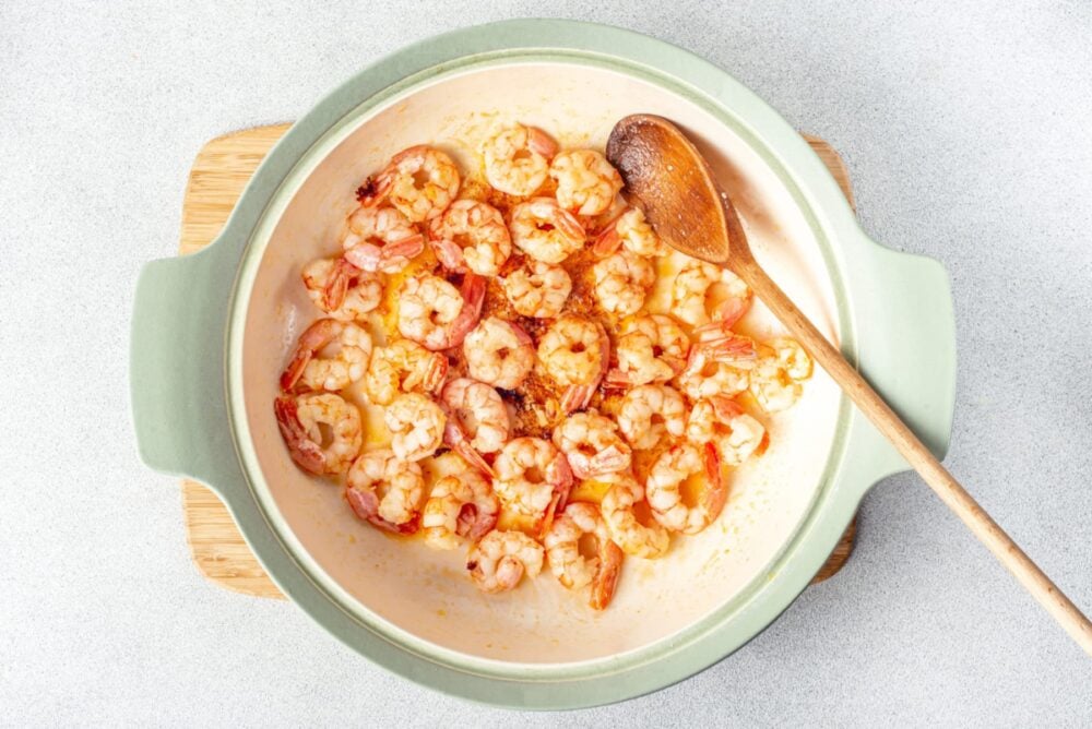 a pot with shrimp on a wooden board with a wooden spoon.