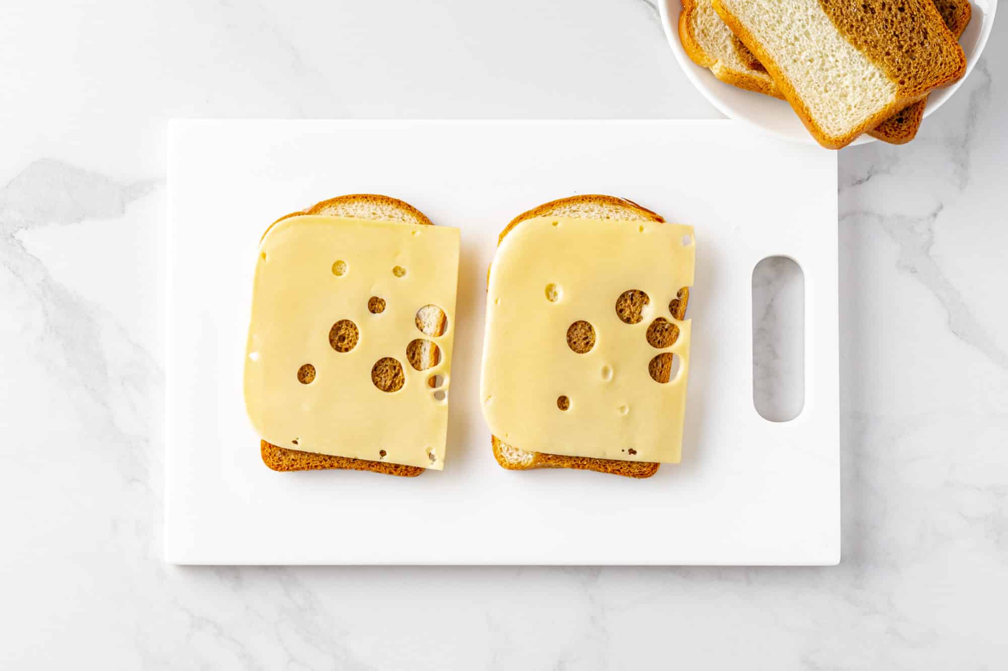 swiss cheese on rye bread on a white board.