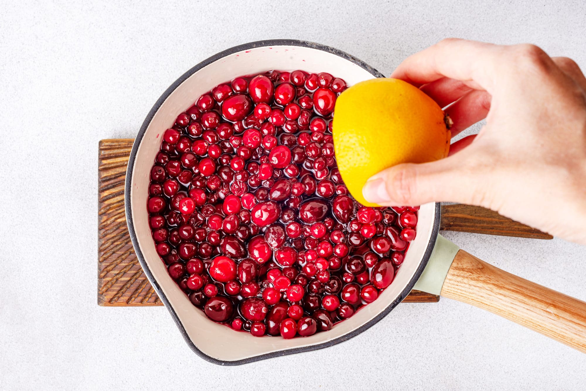 cranberries-and-water-in-a-pot-on-a-wooden-board-with-a-lemon-being-squeezed-into-it