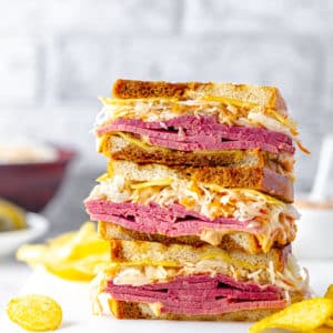 reuben-sandwiches-sliced-and-stacked-on-a-white-board-with-chips-scattered-around