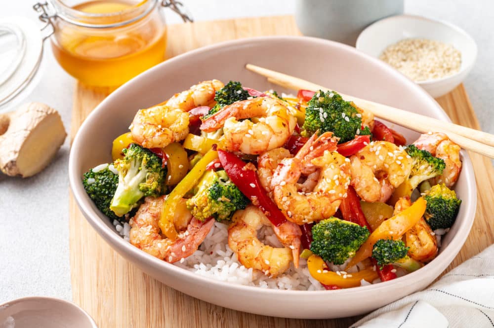 shrimp-stir-fry-over-rice-in-a-dish-on-a-wooden-board-with-chopsticks-on-the-side
