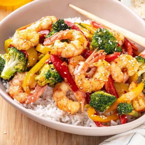 shrimp stir fry over rice in a dish on a wooden board with chopsticks on the side.