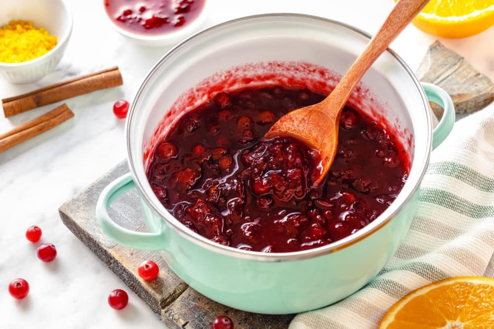 a pot of cranberry sauce with a wooden spoon.