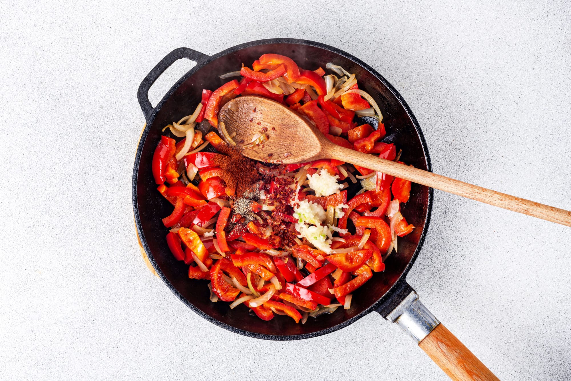 veggies and spices in a black skillet with a wooden spoon.