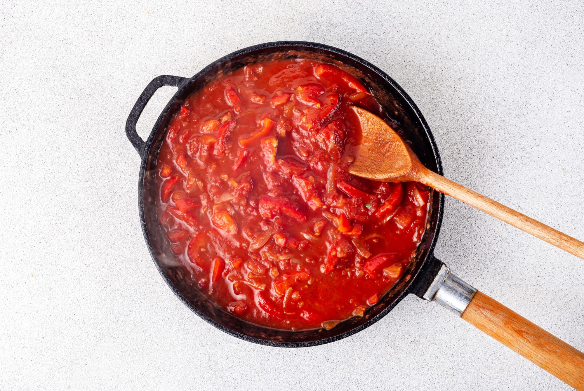 shakshuka base cooking in a black skillet with a wooden spoon in the skillet.