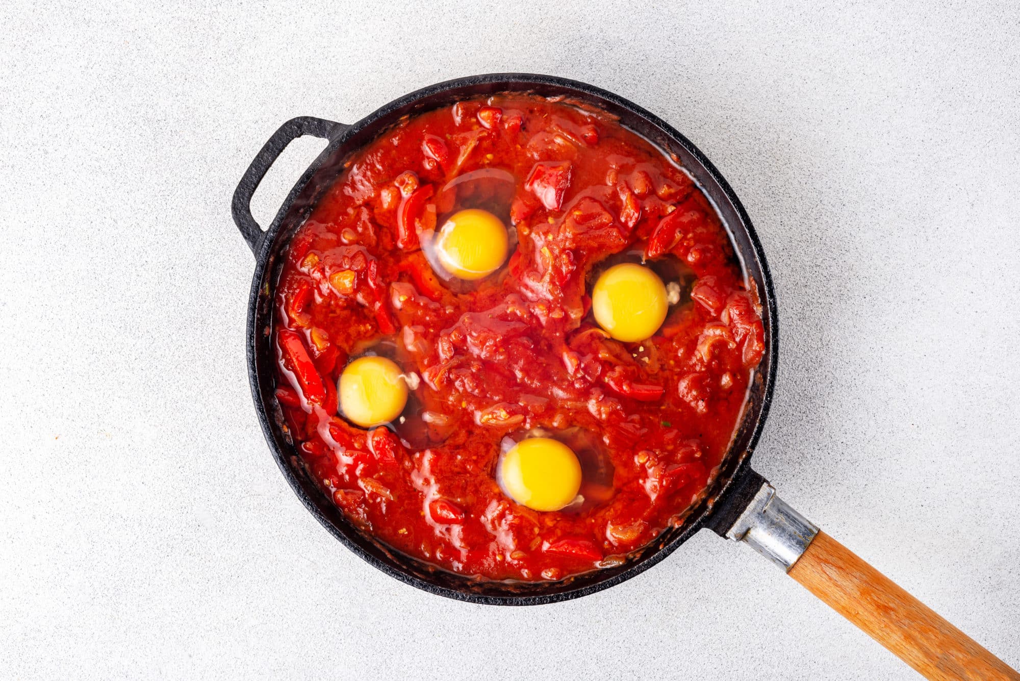 shakshuka base and raw eggs cracked into a skillet.