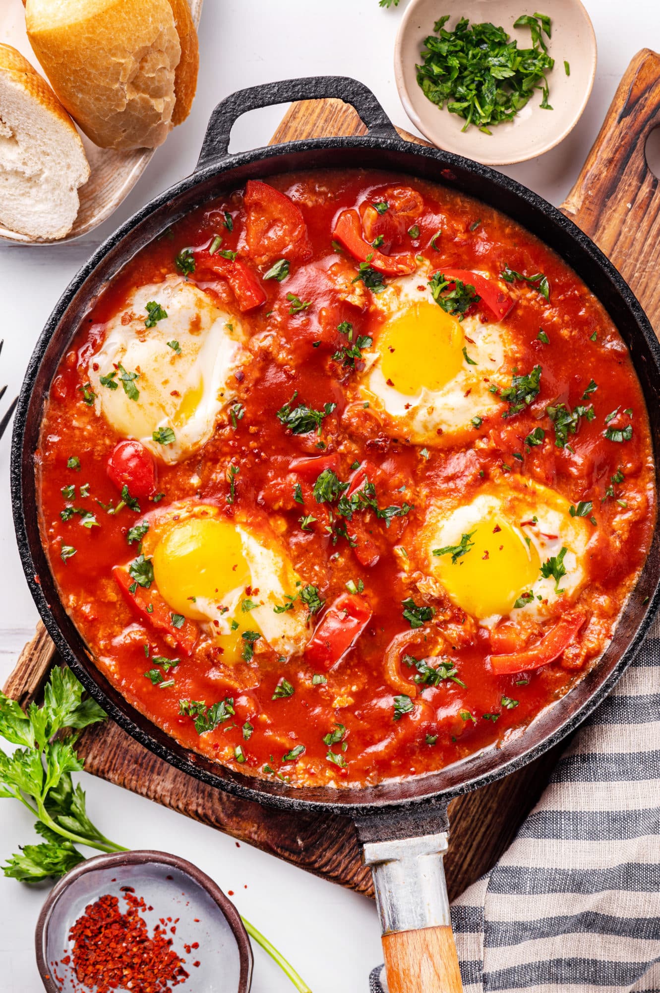 Eggs cooked in a shakshuka base in a skillet with a towel on the side.