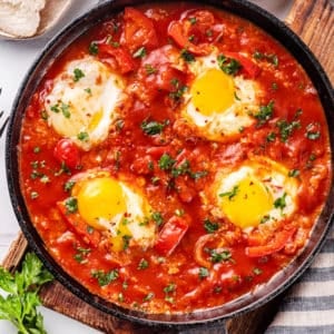 eggs cooked in a shakshuka base in a skillet with a towel on the side.