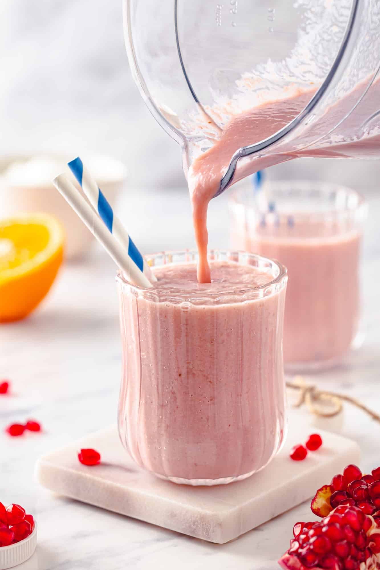 Smoothie being poured into a glass cup with straws from a blender.