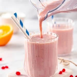 smoothie being poured into a glass cup with straws from a blender.