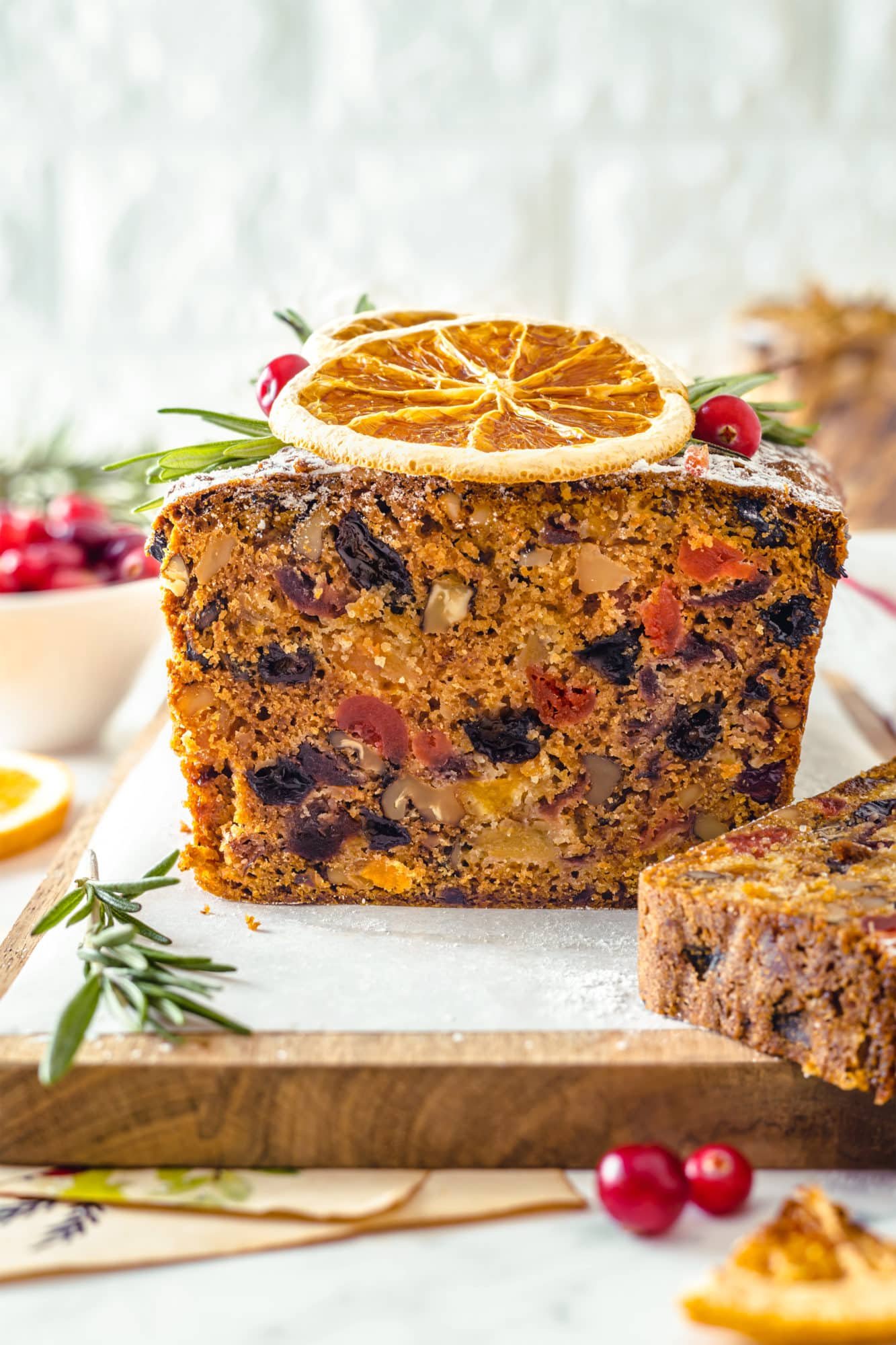 fruit cake side view of the baked inside on a wooden charcuterie board with a rosemary sprig on the side.