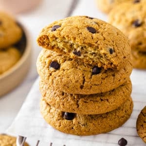 chocolate chip cookies stack with the top cookie as a half stacked on parchment paper and a cooling rack.