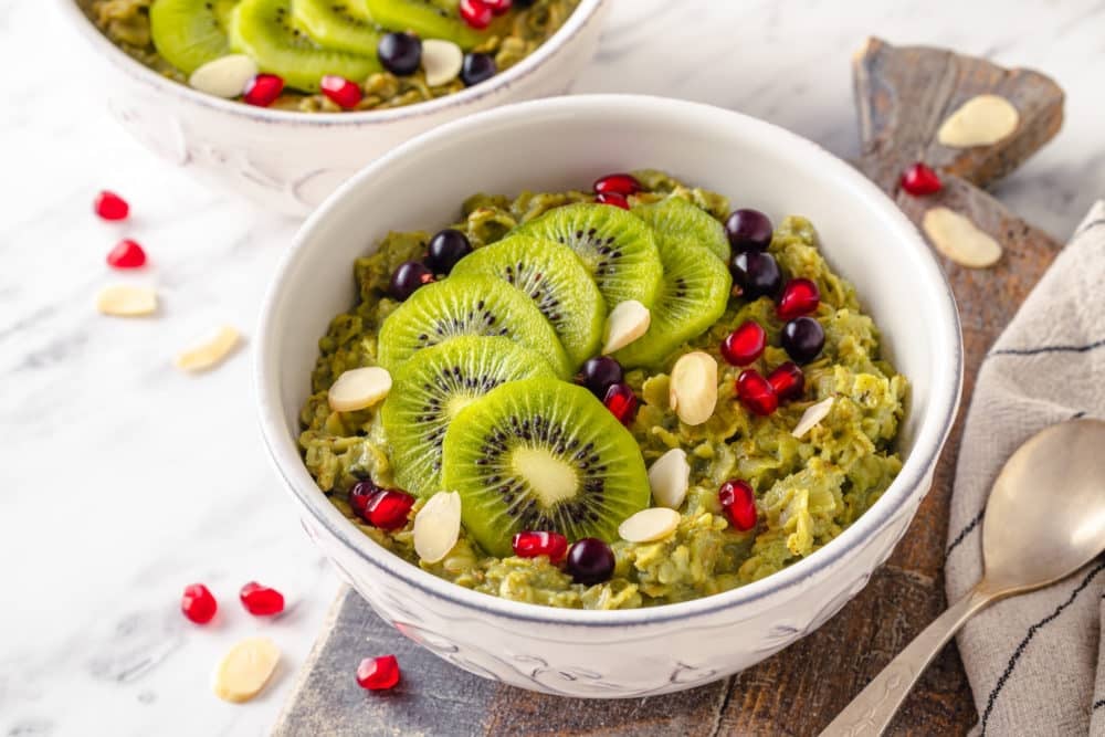 matcha-oatmeal-in-a-white-bowl-on-a-wooden-board-with-a-spoon-and-ingredients-scattered-around