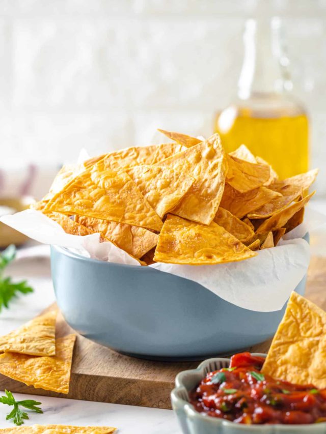 tortilla chips in a blue bowl with parchment paper in the bowl on a wooden board.