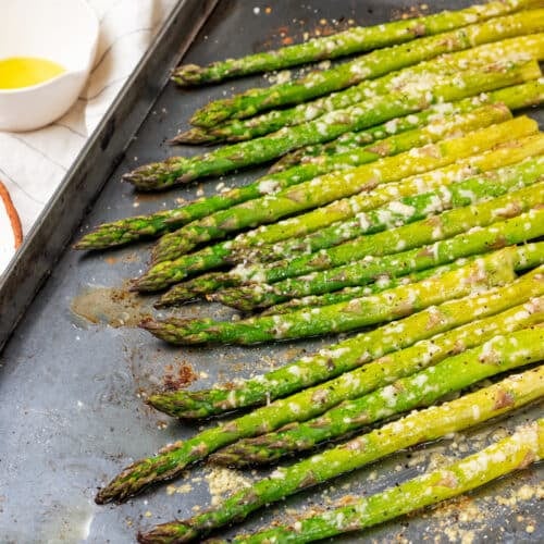 a baking sheet with baked asparagus on it.