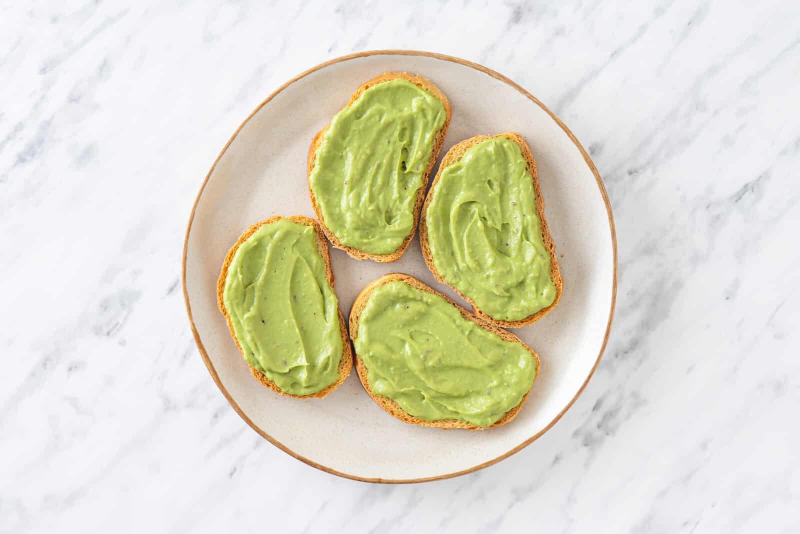 slices of toast on a white plate with avocado topping on each slice.