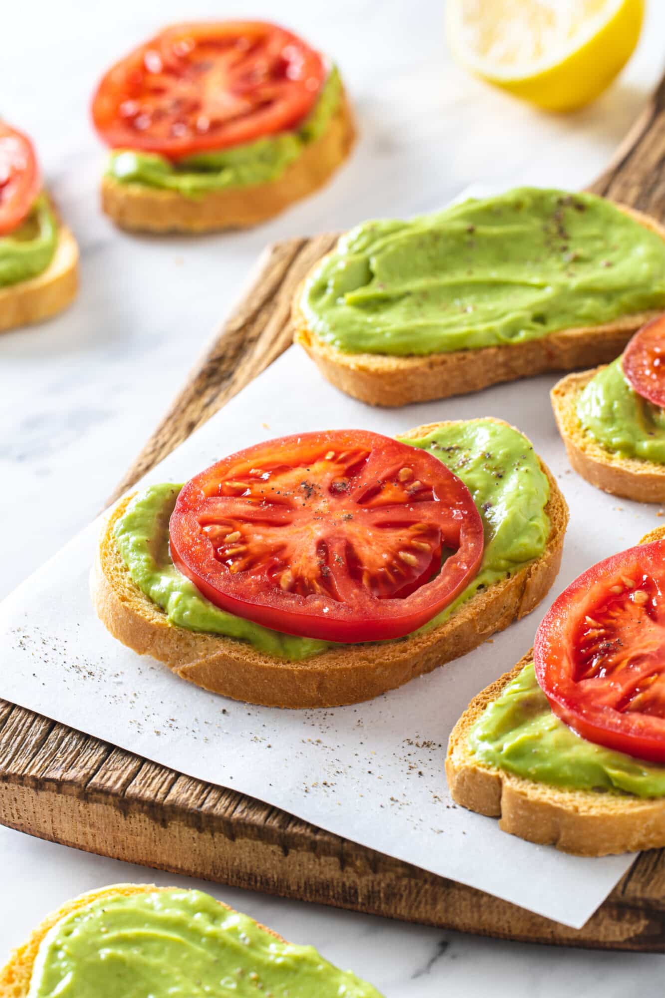 appetizers on parchment paper on a wooden board with a slice of tomato on each avocado toast.