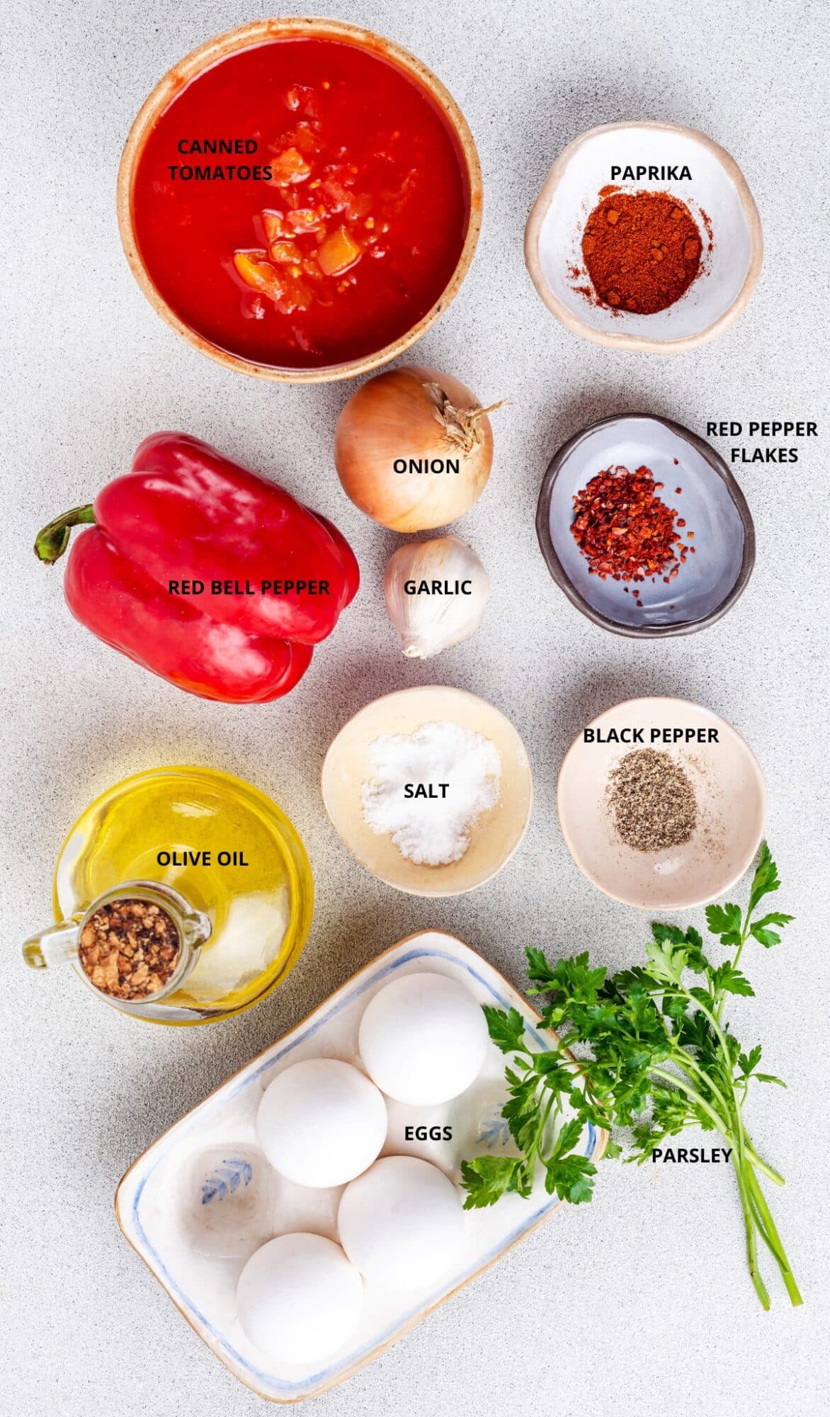 shakshuka recipe ingredients labeled paprika canned tomatoes red pepper flakes onion garlic red bell pepper olive oil salt black pepper eggs and parsley.