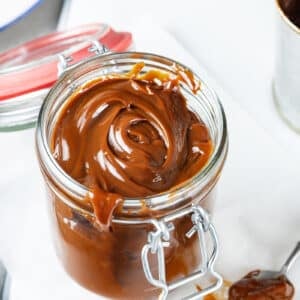 sweet dulce de leche in a glass jar with the lid open and a spoon of the leche on the table.