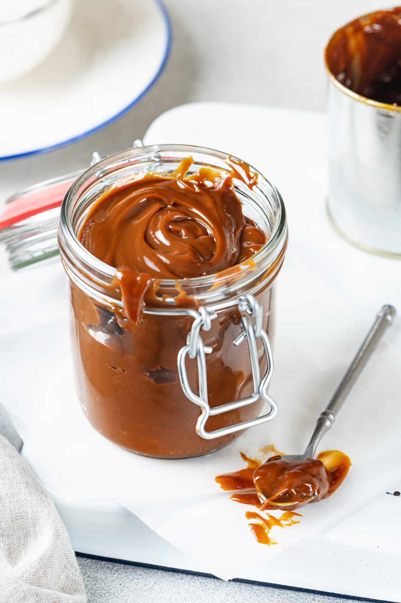 dulce de leche in a jar made of glass with another spoon of it on a piece of parchment paper.