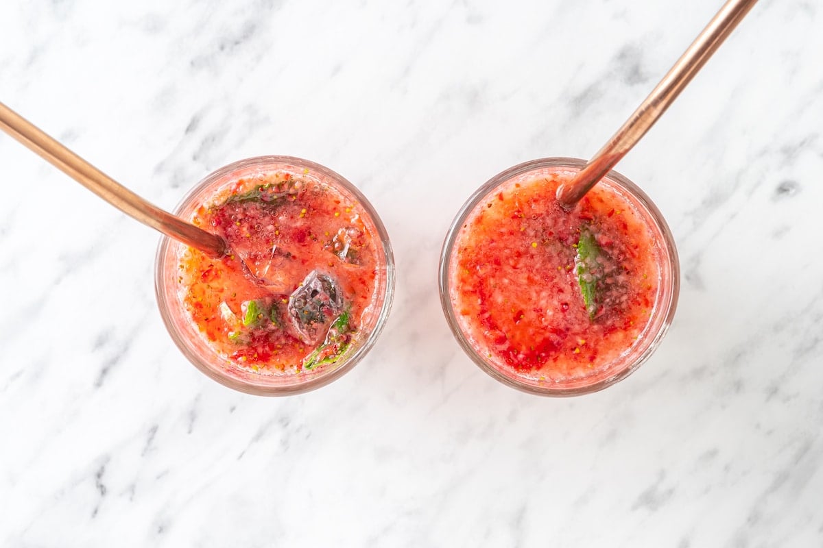 blended strawberries in two glass cups with fresh mint lime juice ice and club soda.