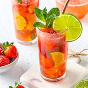 strawberry mojito mocktail prepared in a several glasses with strawberry and lemon slices inside with mint and lime slices on top with straws and more strawberries scattered around.