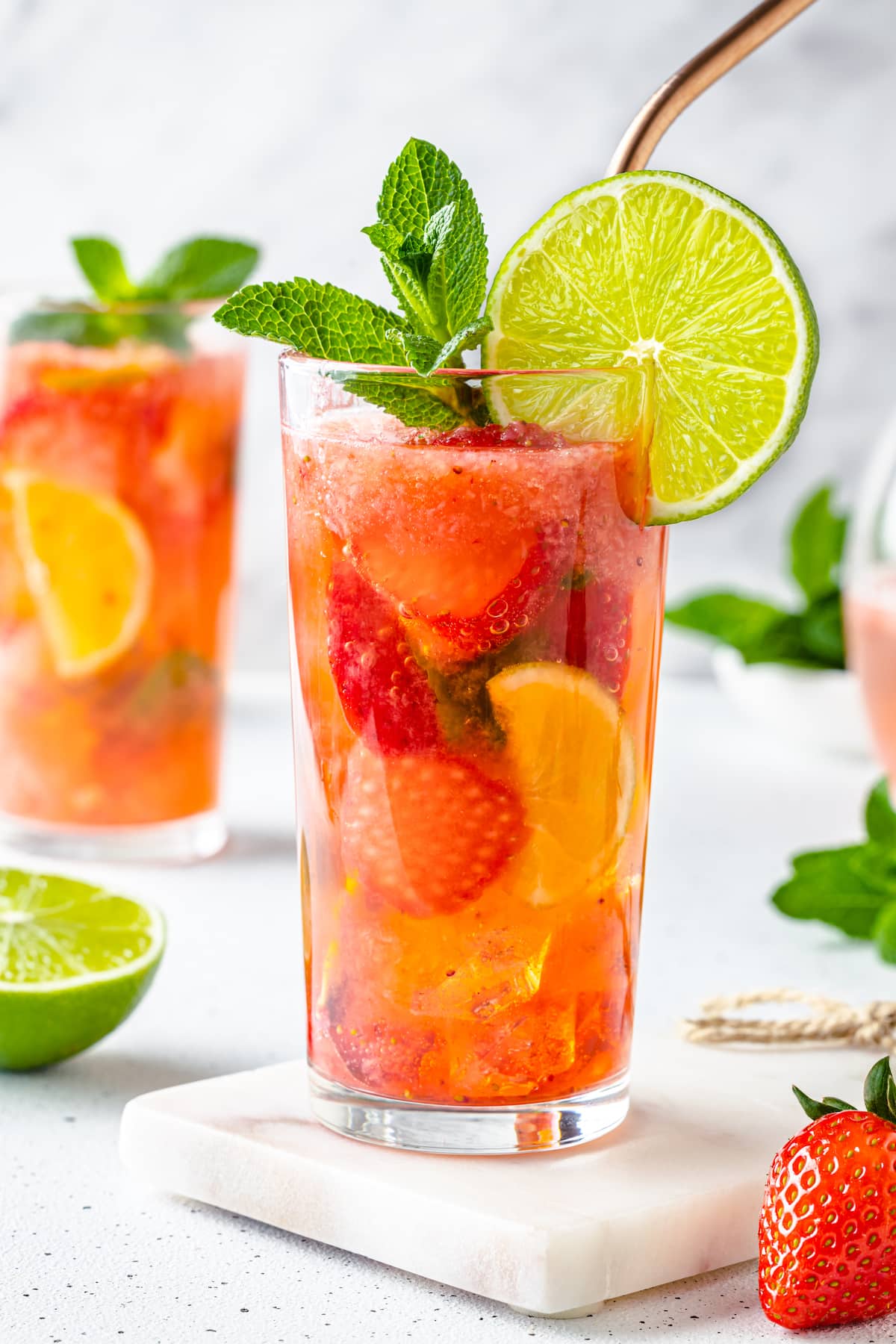 clear glass on white board filled with lime juice fresh mint and strawberries with sparkling water.