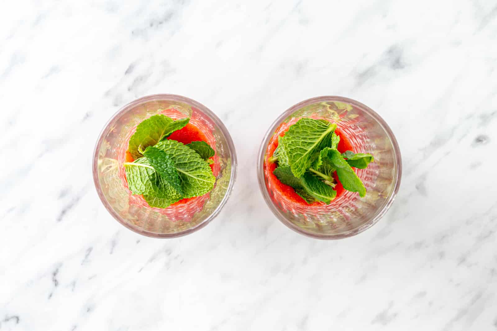 blended fresh strawberries in two glass cups and fresh mint leaves.

