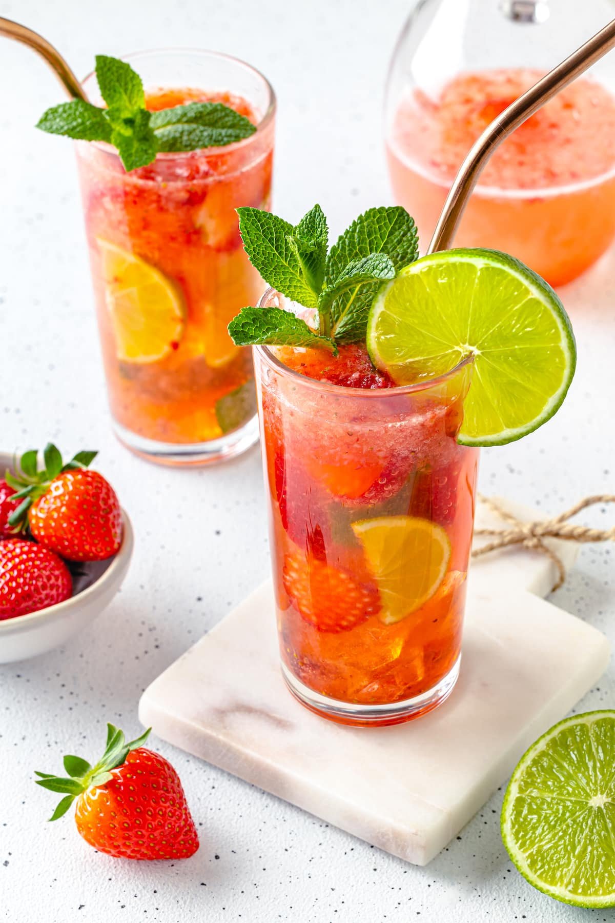 clear glass on white board filled with lime juice fresh mint and strawberries with sparkling water.