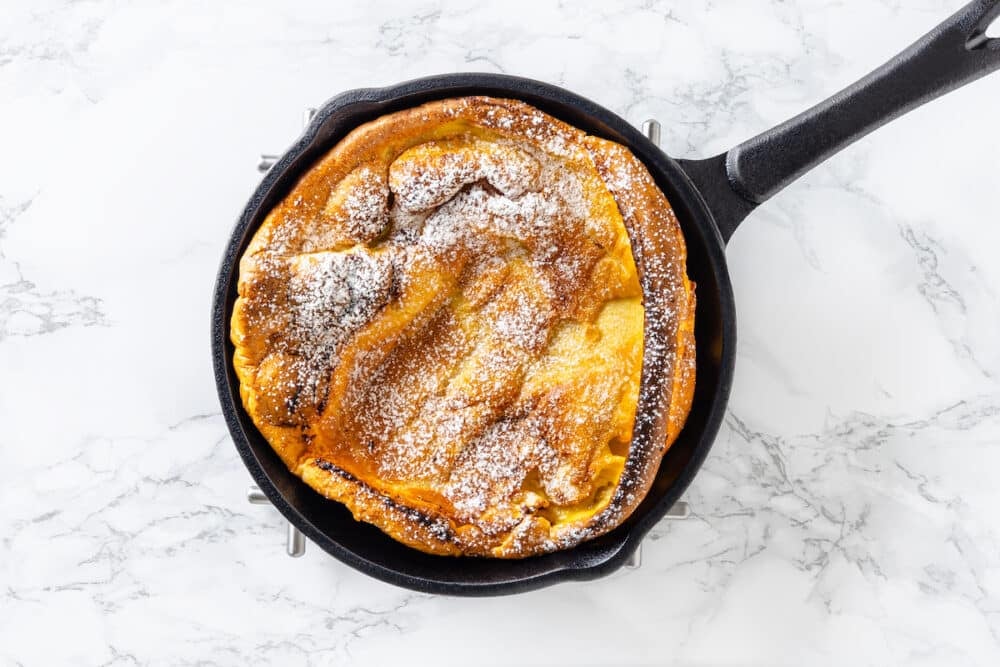 a dutch baby pancake baked and inflated with powdered sugar sprinkled on top.