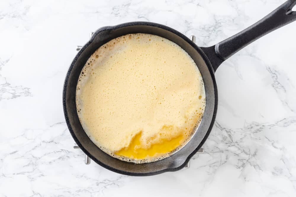 dutch baby pancake batter with butter in a cast iron skillet.