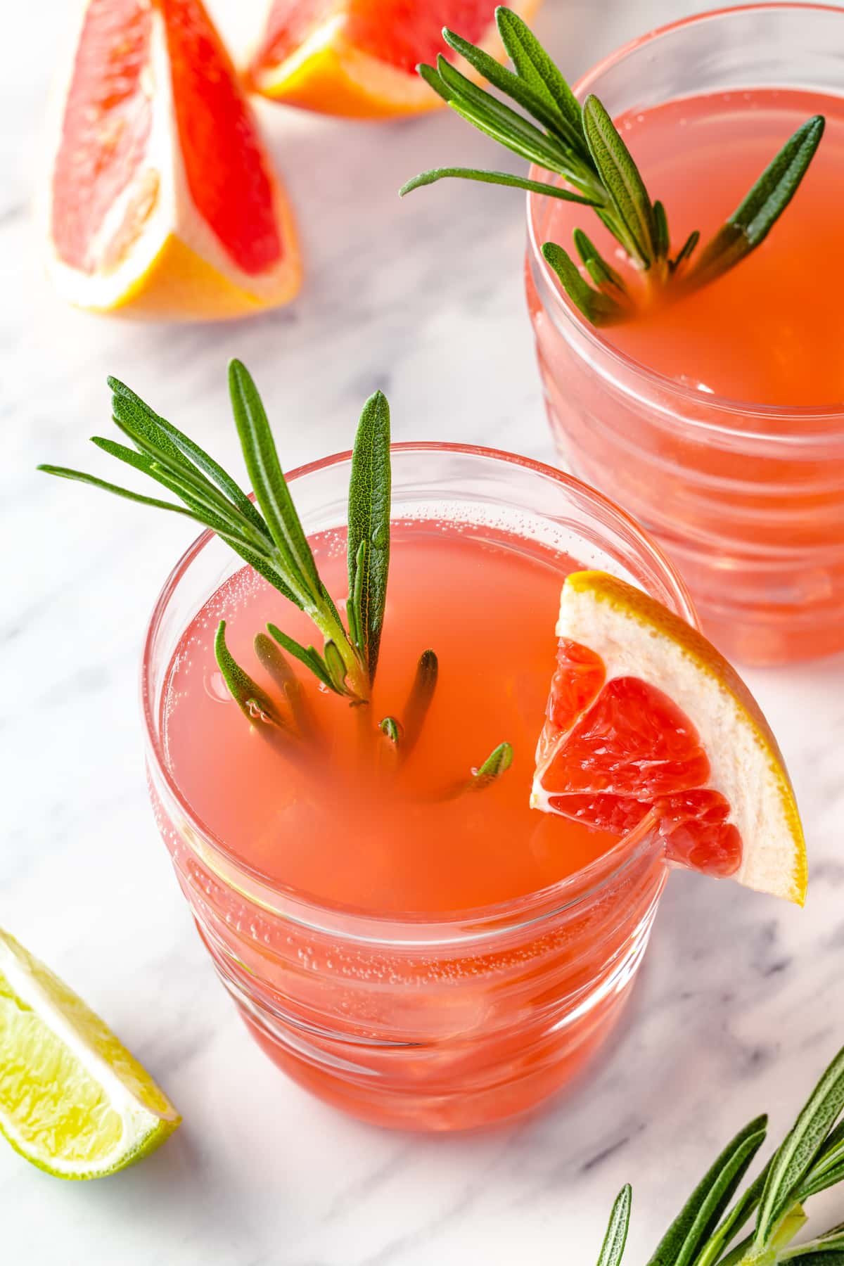 Close up overhead shot of a glass of grapefruit lime drink with rosemary simple syrup. there's a lime to the side, rosemary sprigs garnishing the drink, and a wedge of grapefruit