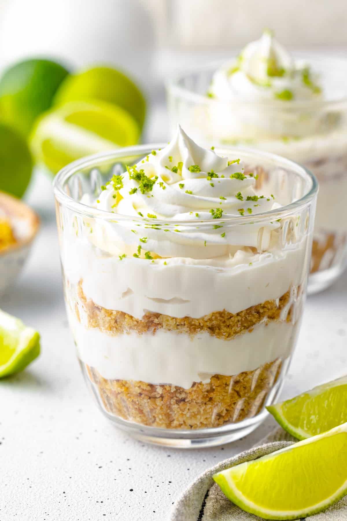 Key lime dessert with crumbs whipping cream and lime zest in clear cup.