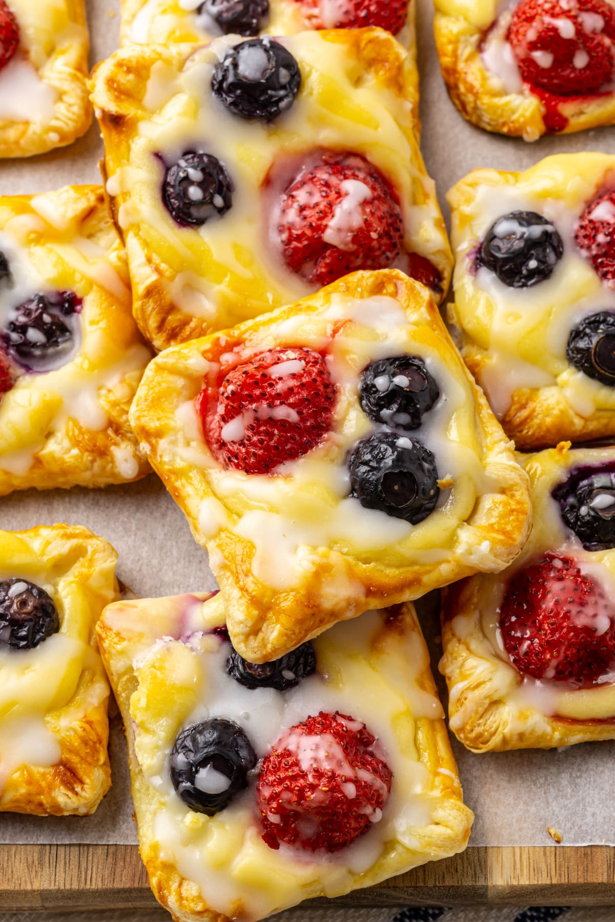 overhead close up view of cream cheese danish squares with icing and berries on top