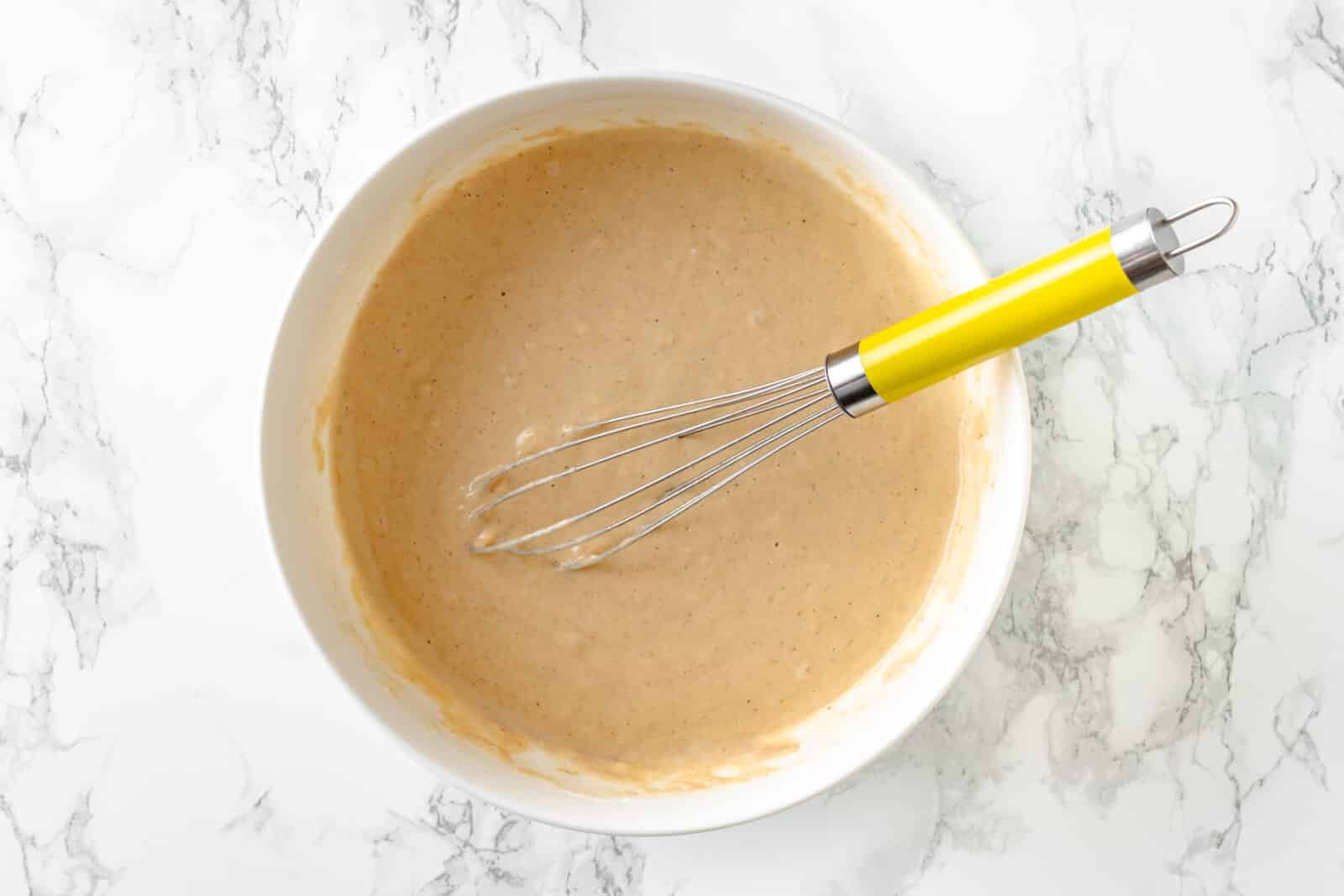 white bowl full of pancake batter with a yellow whisk resting inside 