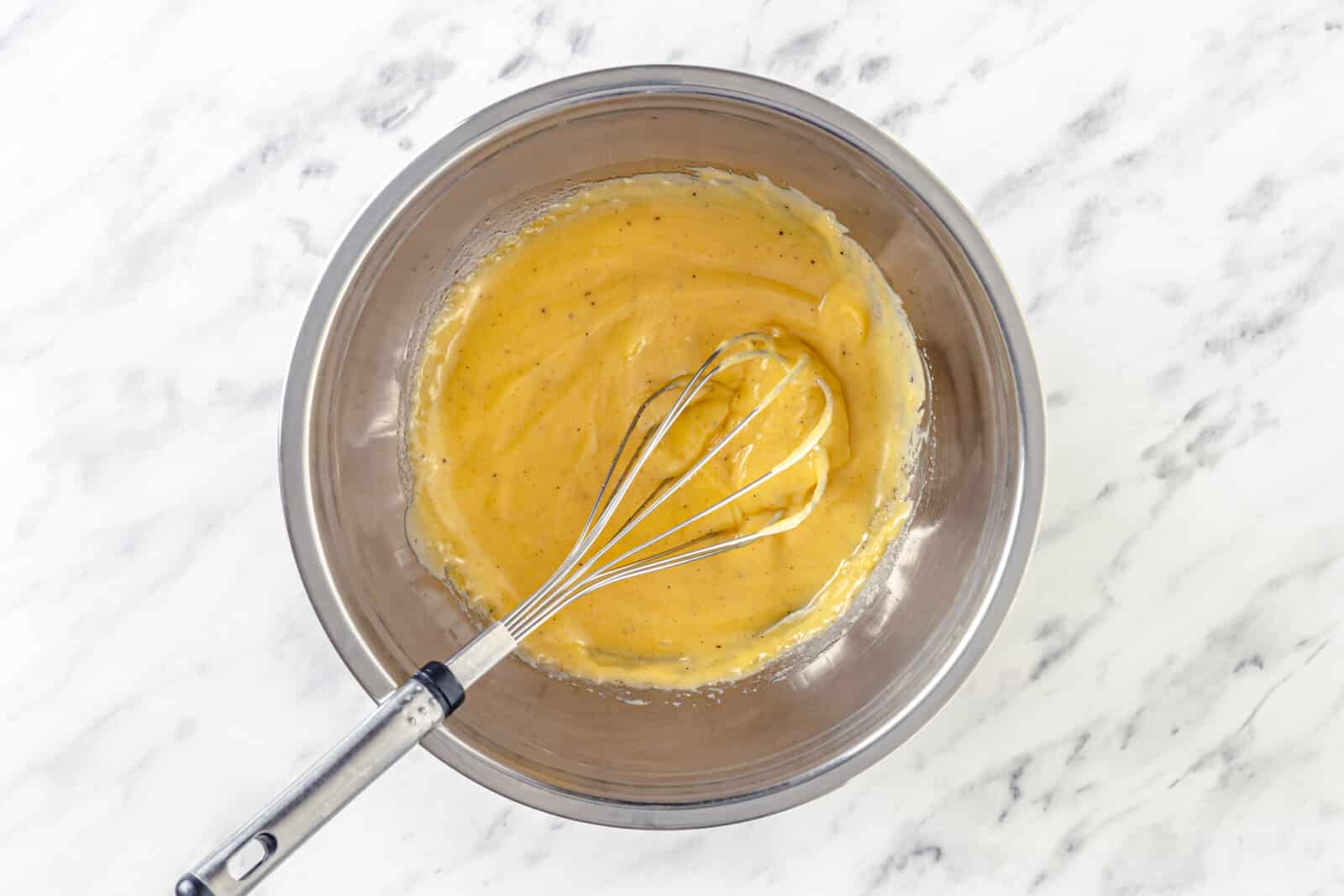 a silver bowl full of hollandaise sauce with a whisk in it