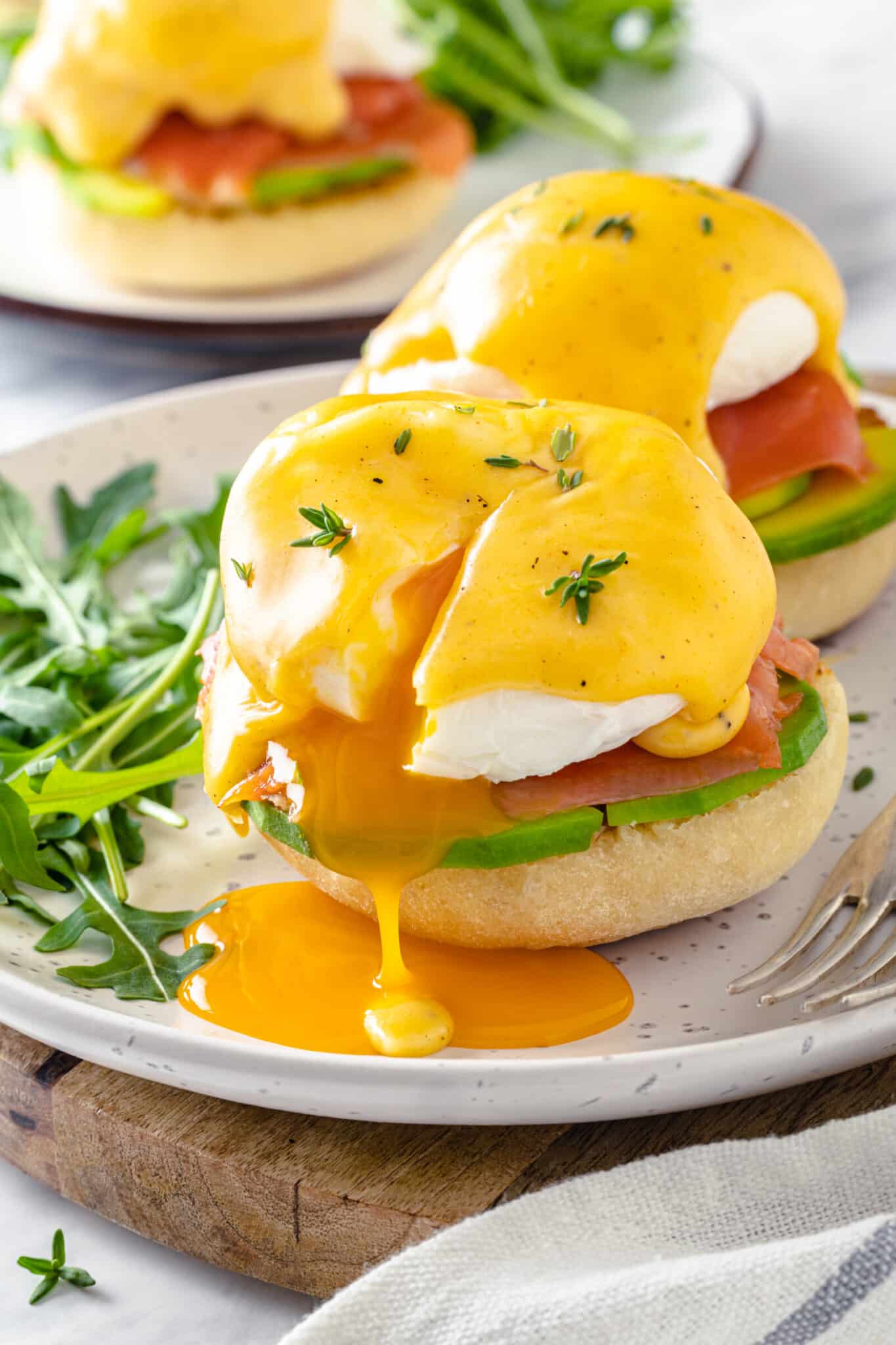 a white plate serving smoked salmon eggs benedict with the poached egg leaking yolk
