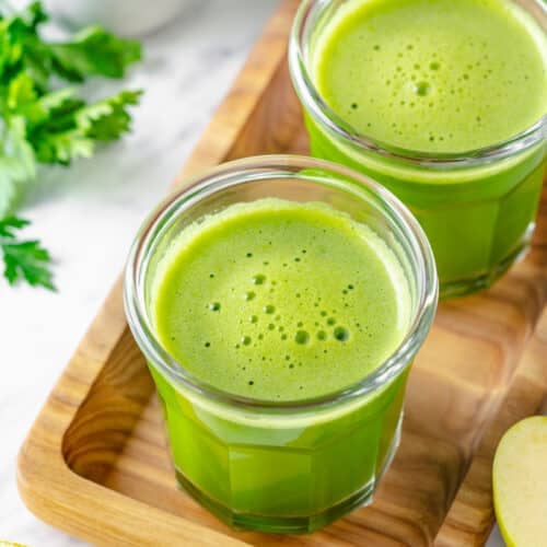 Green juice in two glasses atop a decorative tray.