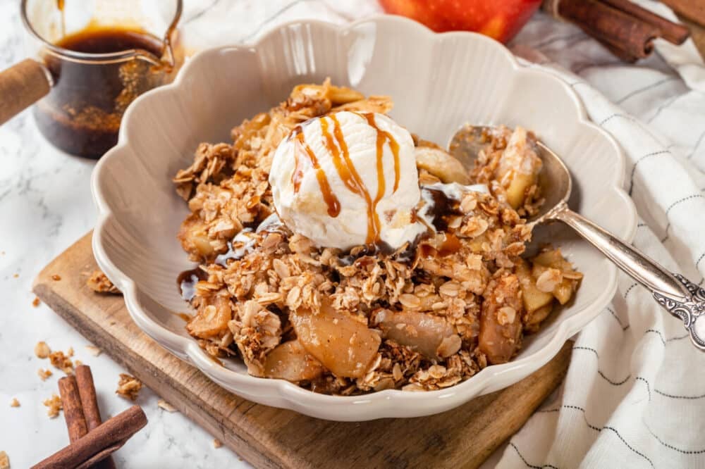 Gluten free apple crisp in a bowl, topped with ice cream and caramel sauce.